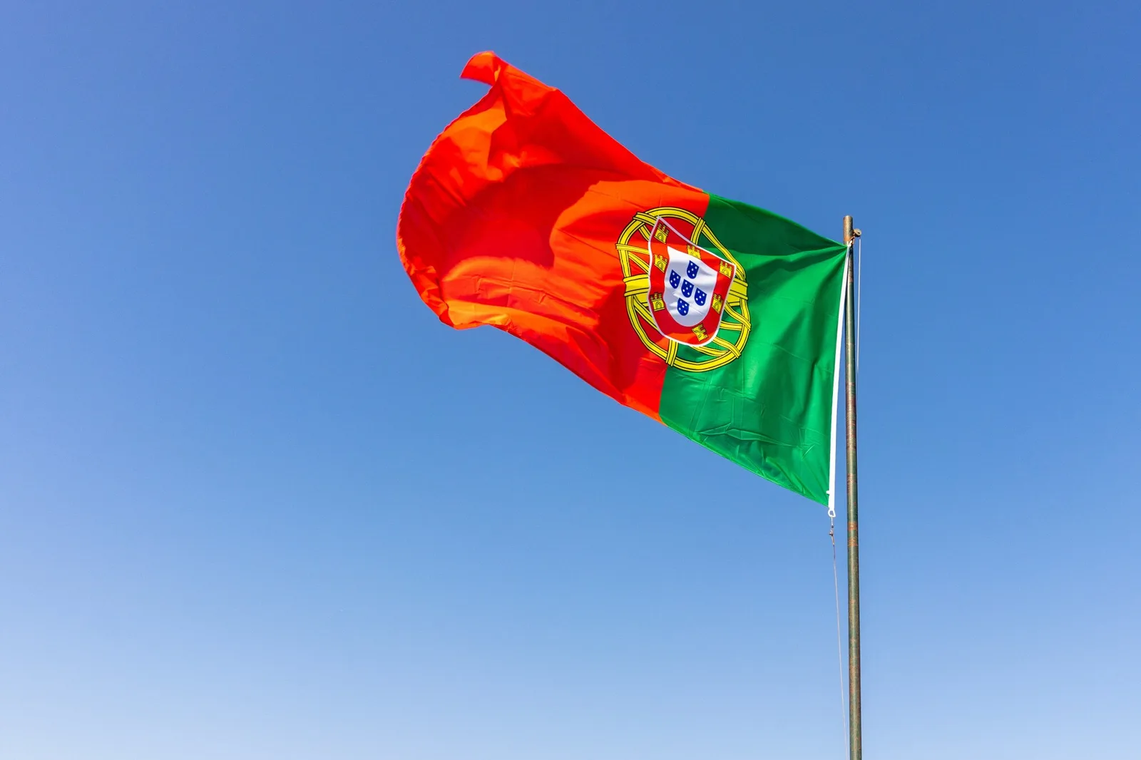 Bandeira de Portugal tremulando em um mastro contra o céu azul