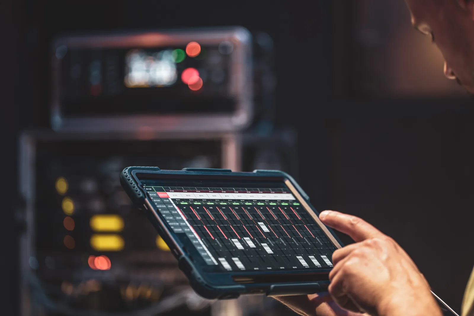 Técnico acompanha painel de monitoramento em um tablet diante de equipamentos montados em rack