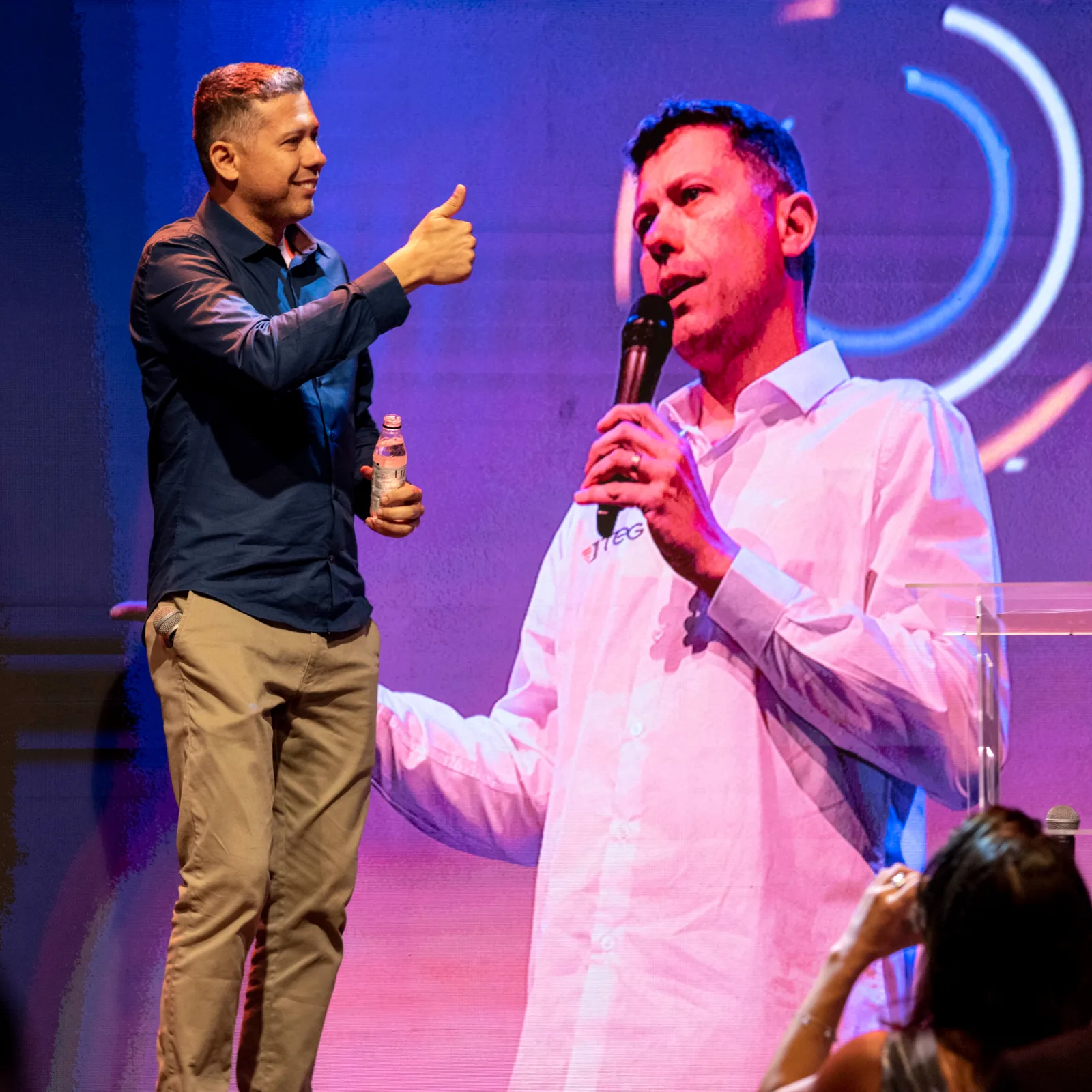 Dois palestrantes ao microfone no palco de um evento da TEG