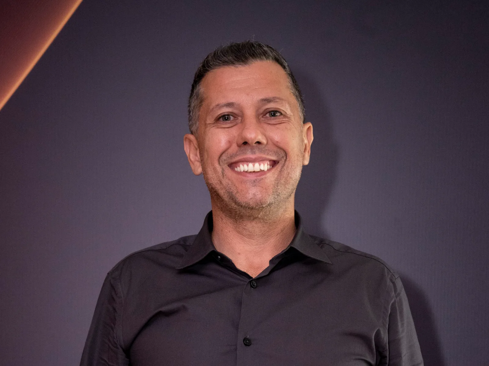 Rafael Galasso sorrindo em retrato, com fundo escuro