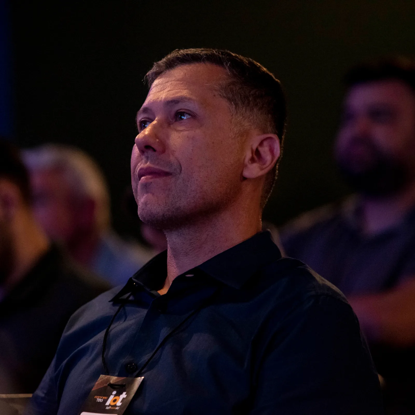 Rafael Galasso sorrindo na plateia de um evento, ao lado de outro participante